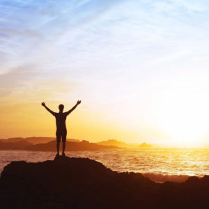 A person standing on top of a rock near the ocean.